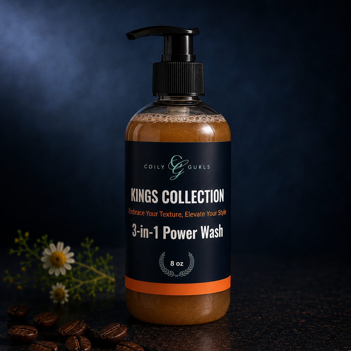 A pump bottle of Coily & Gurls Kings Collection 3-in-1 Power Wash, filled with brown hair product, set on a dark textured surface with coffee beans and small white flowers against a dark blue background.